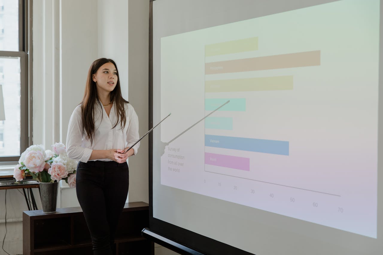 Woman in white blouse presenting data on a projector screen in a modern office setting.